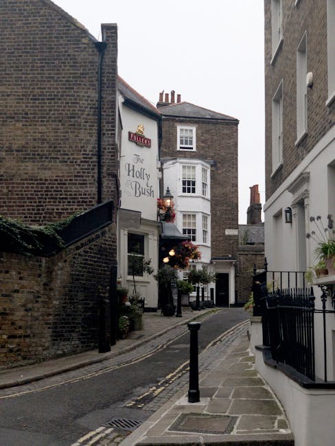 A close-up view of a brick exterior wall displaying a rectangular metal street name sign with white lettering that reads 'LOWER TERRACE NW3,' attached to the wall with visible screws. The bricks are d